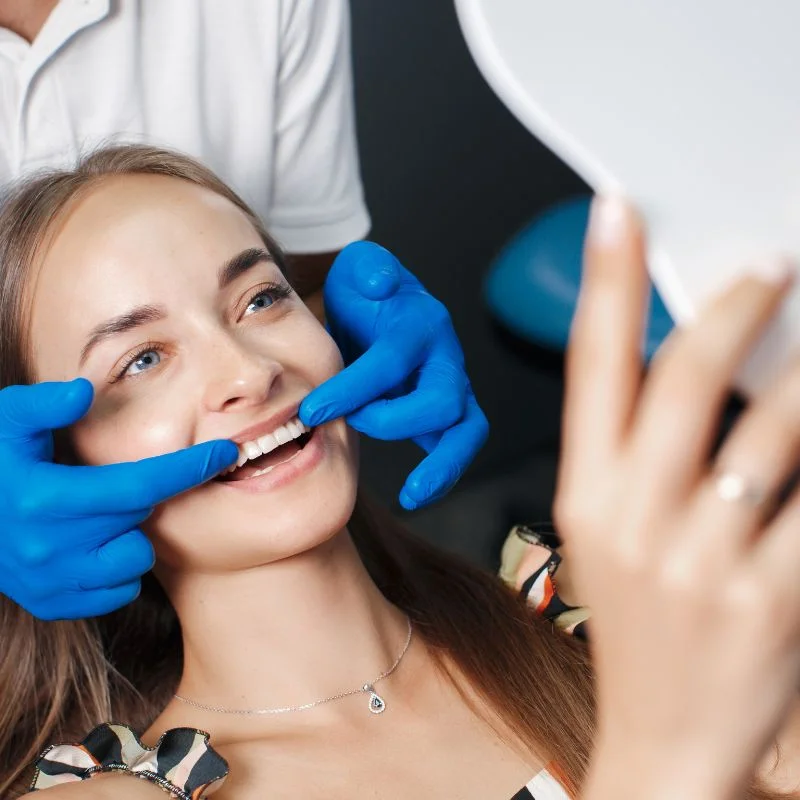 Teenage girl smiling while holding mirror after professional teeth whitening treatment at Fairmont Dental Centre
